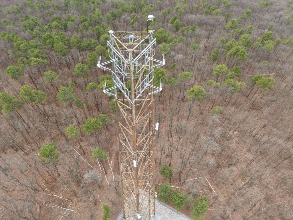 Aerial drone inspection of a lattice communications tower over woodland